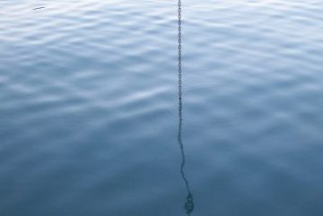 A stock image of a chain dropping into a still, blue ocean.